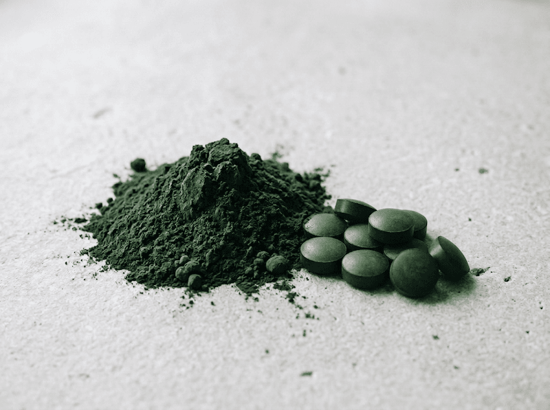 Organic chlorella in powder and pill forms on a white stone bench